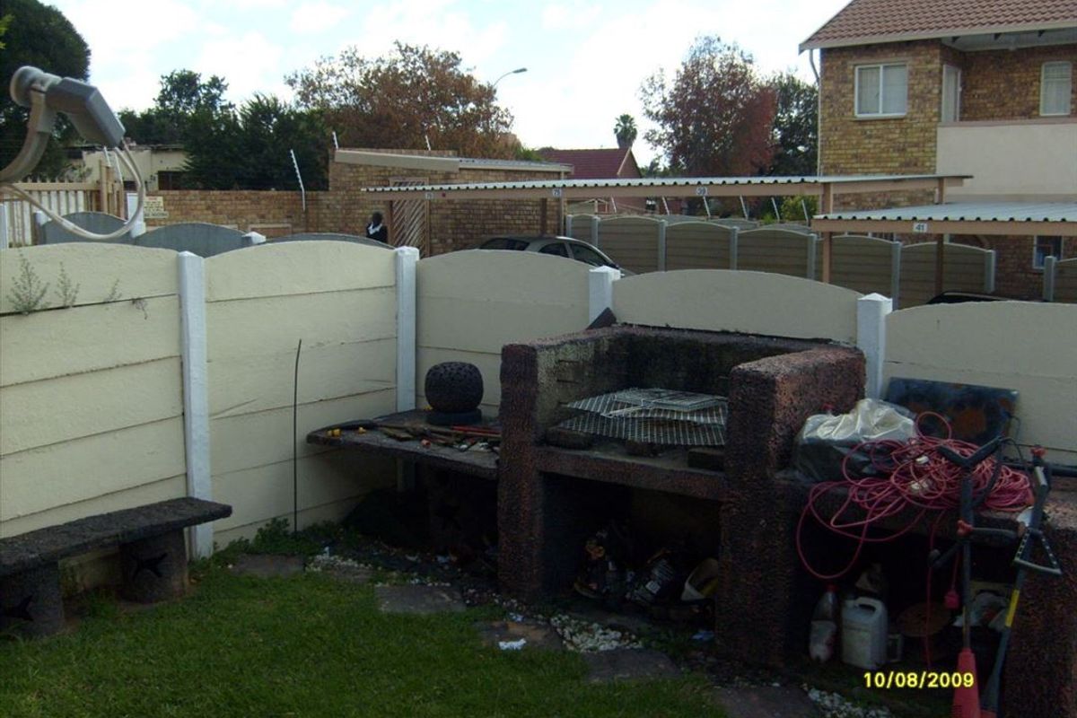 Rear garden area featuring a built-in brick braai, concrete bench seating, and perimeter precast concrete walling.