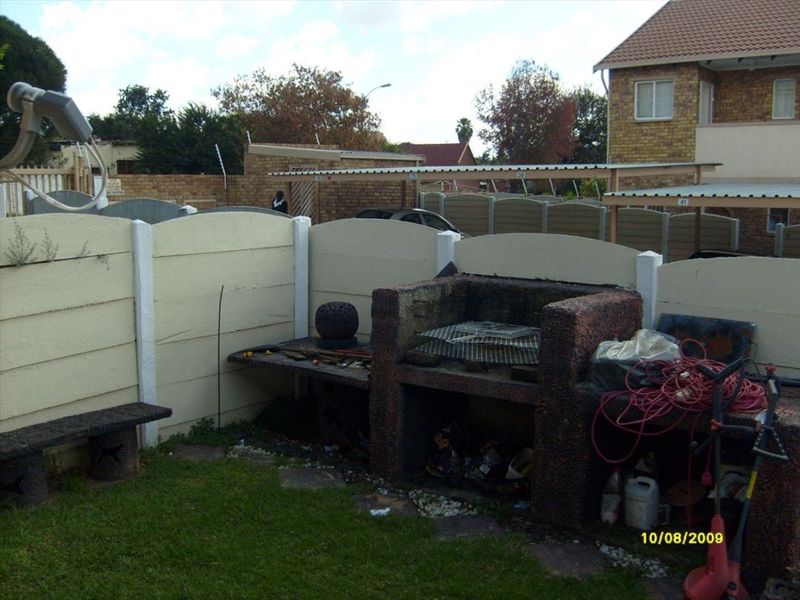 Rear garden area featuring a built-in brick braai, concrete bench seating, and perimeter precast concrete walling.