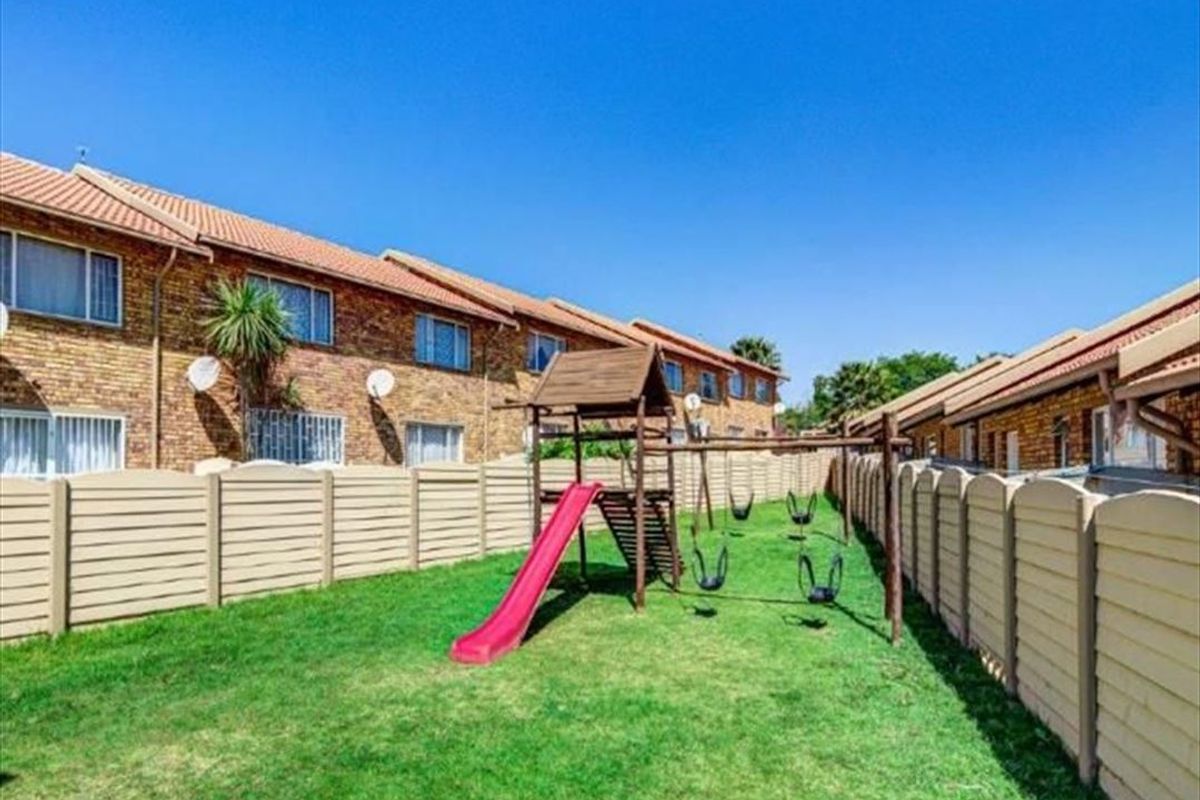 A communal garden area featuring a lawn, precast concrete boundary walls, and a children's play structure set against a brick townhouse complex.