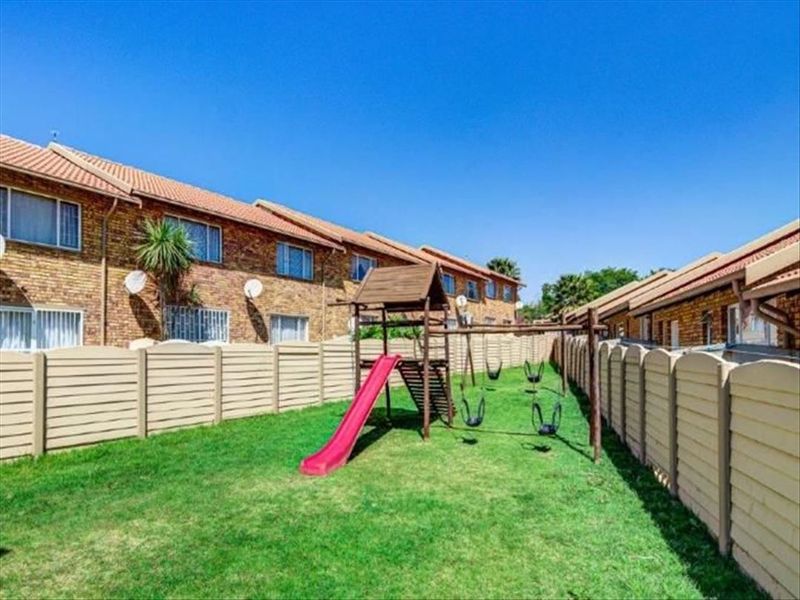 A communal garden area featuring a lawn, precast concrete boundary walls, and a children's play structure set against a brick townhouse complex.