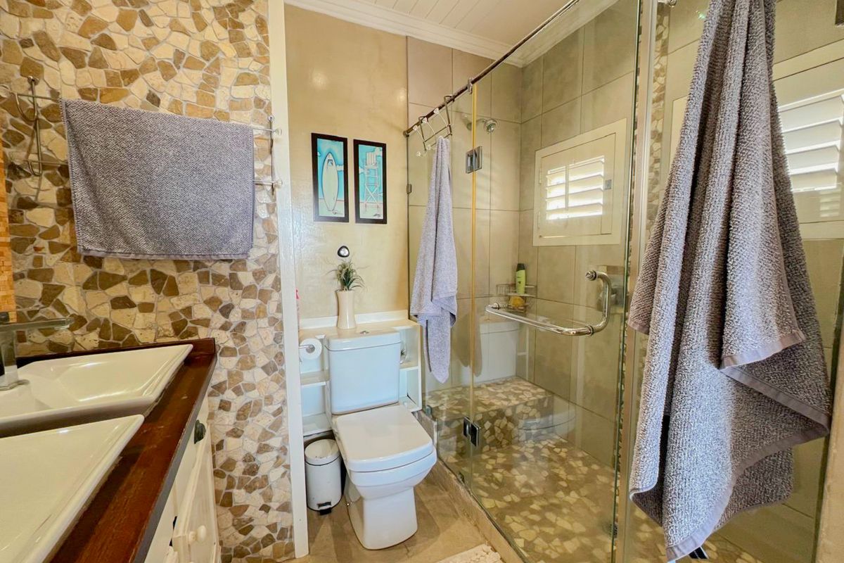 Bathroom featuring a stone mosaic feature wall, dual vessel sinks on a wooden vanity, and a glass-enclosed shower with stone flooring.