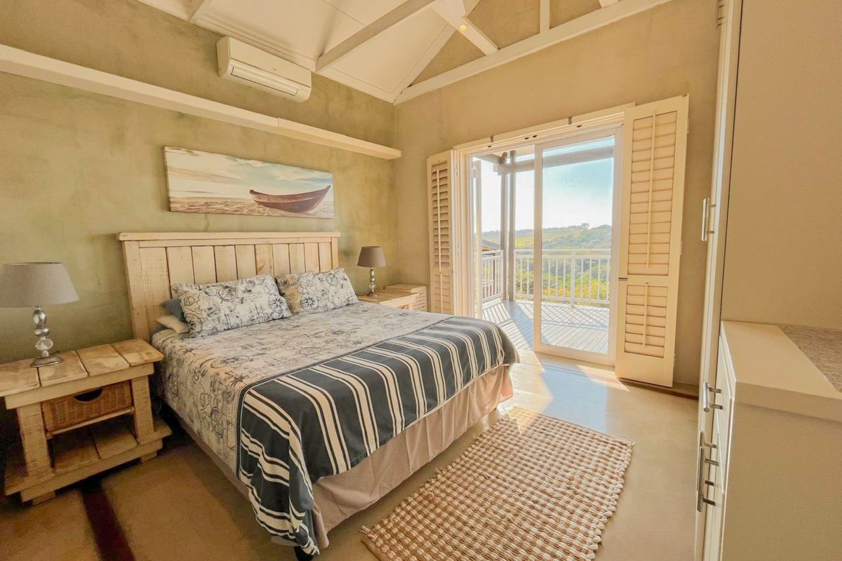 Spacious bedroom featuring a vaulted ceiling with exposed rafters, split-system air conditioning, and sliding glass doors opening onto a private balcony with plantation shutters.