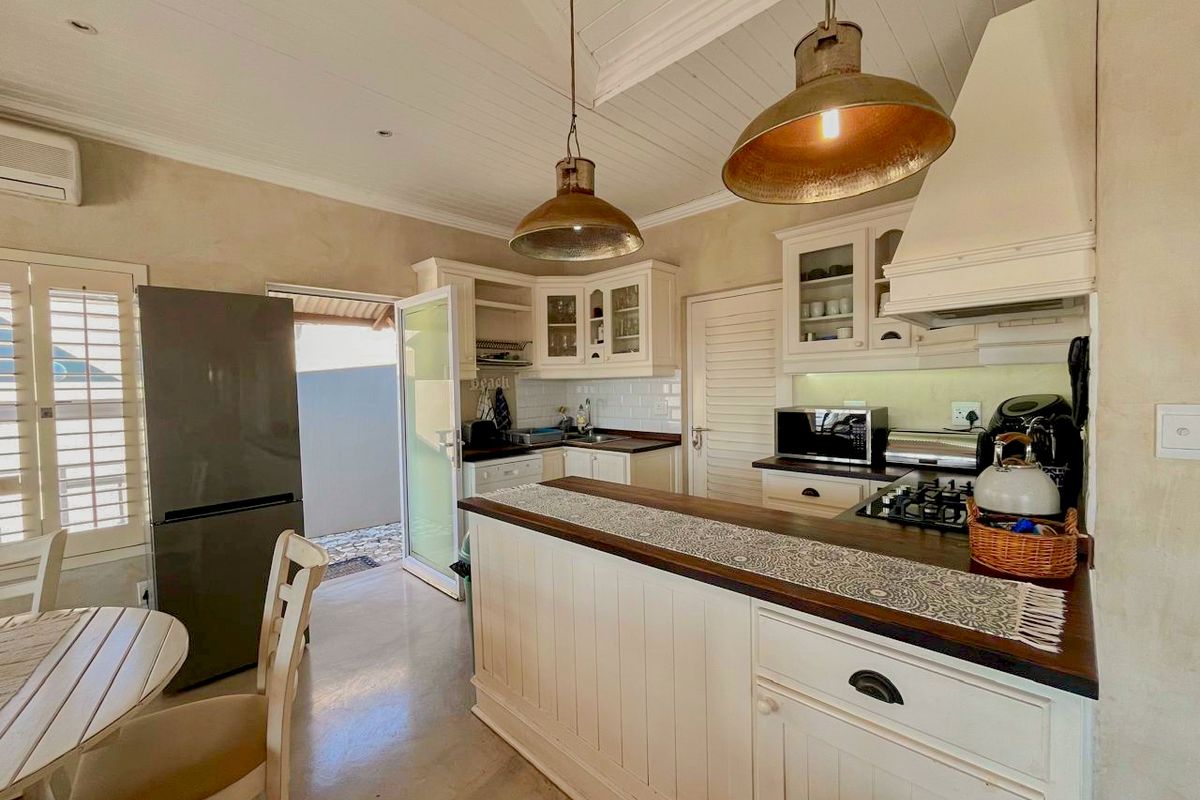 A charming kitchen featuring white cabinetry, timber countertops, a gas hob, and a subway tile backsplash, with direct access to an outdoor area.