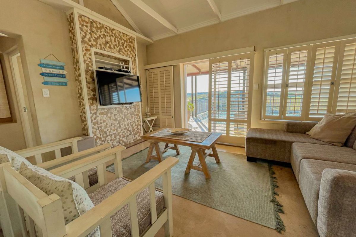 A bright living room featuring a vaulted ceiling, stone accent wall, and plantation shutters, with direct access to an outdoor patio area.