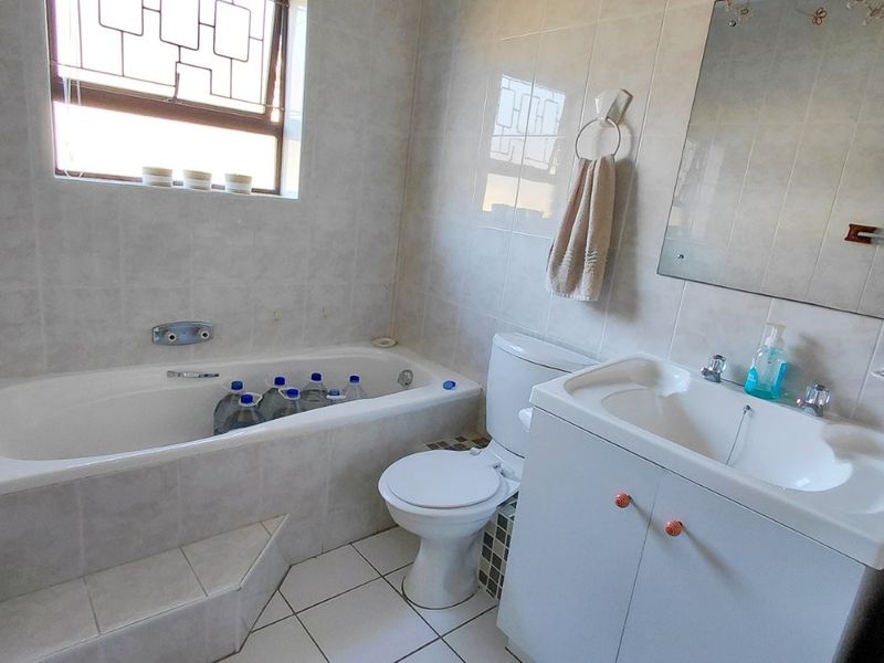 A functional bathroom featuring a built-in bathtub, vanity cabinet with basin, and tiled finishes throughout, including security bars on the window.