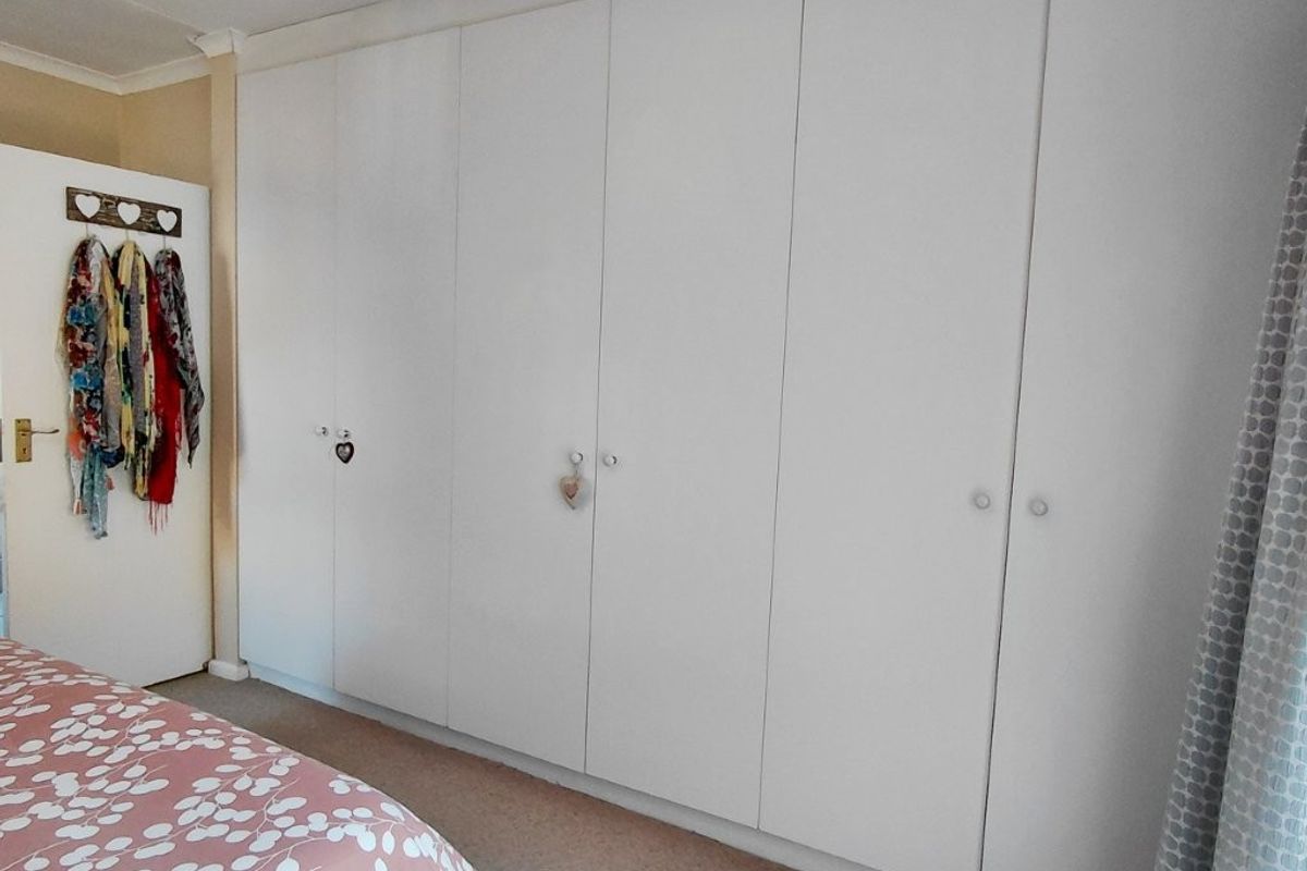 A bedroom featuring a wall-to-wall built-in cupboard unit with white cabinetry.