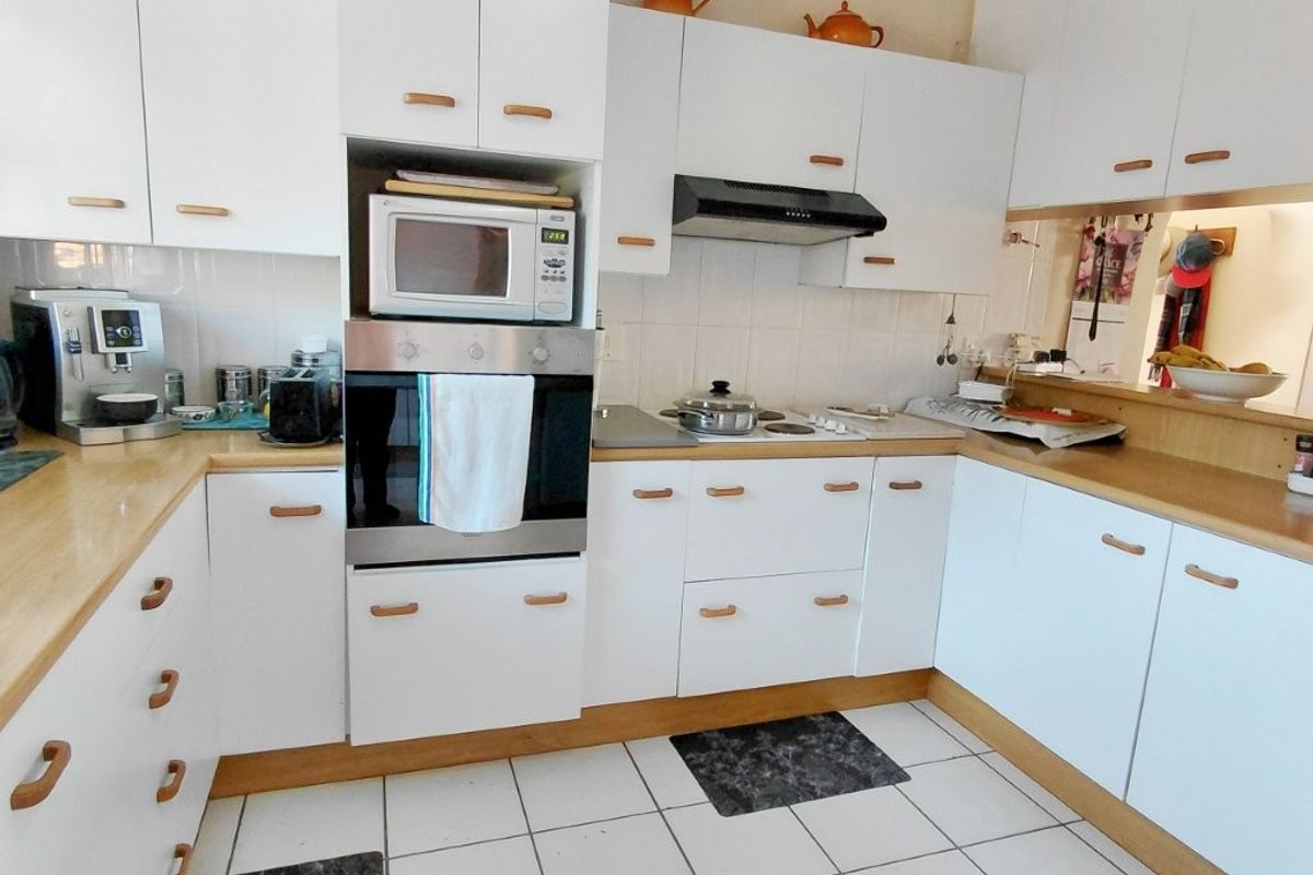 A functional kitchen featuring white cabinetry, laminate countertops, built-in oven, microwave, and an extractor fan, complemented by tiled flooring.