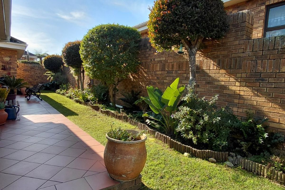 A well-maintained rear garden featuring a tiled patio area, established landscaping, and a solid brick boundary wall.