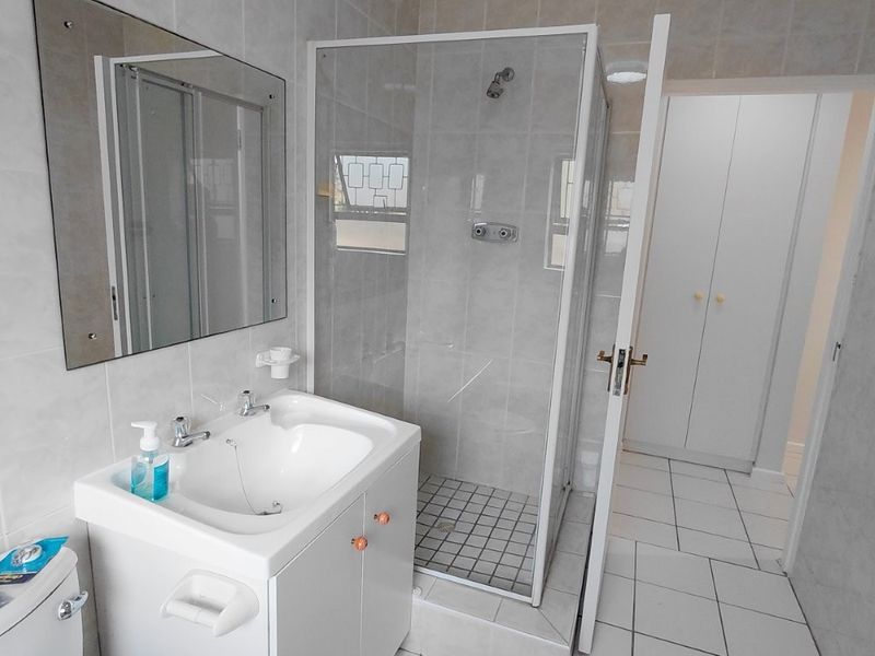 A functional bathroom featuring a vanity cabinet, a glass-enclosed shower, and neutral wall tiling, with adjacent built-in storage cupboards.