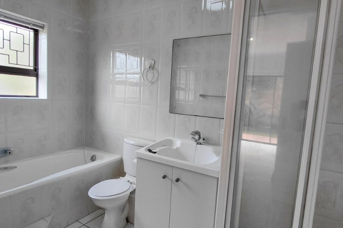 A functional bathroom featuring a bathtub, separate shower enclosure, vanity with basin, and toilet, finished with neutral wall and floor tiles.
