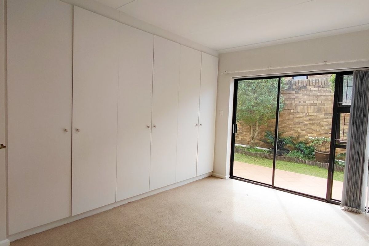 A bright, empty bedroom featuring extensive built-in cupboards and a sliding glass door providing direct access to a private rear garden area.