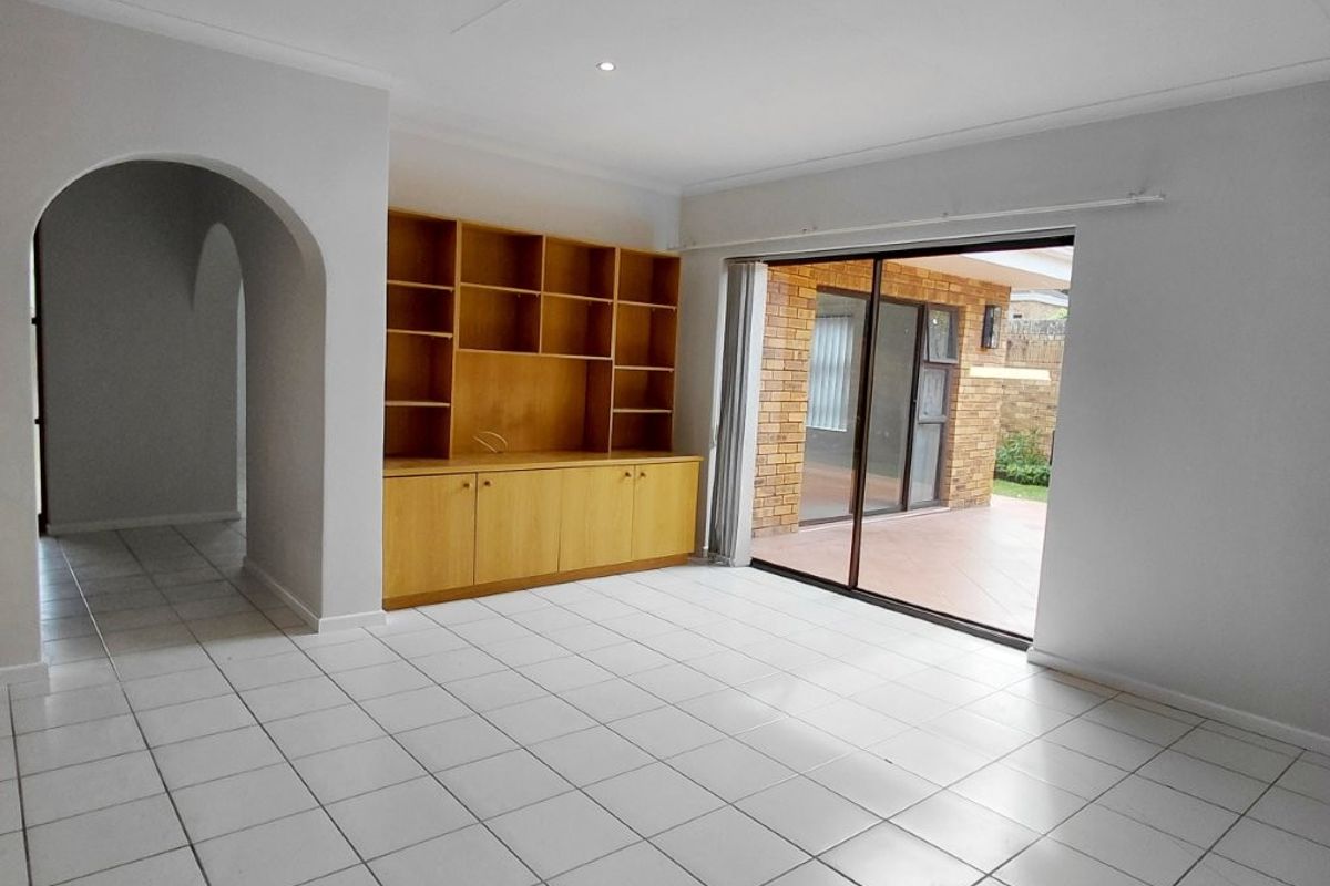Spacious living area featuring neutral tiled flooring, a built-in wooden shelving unit, and large sliding glass doors providing access to the outdoor patio.
