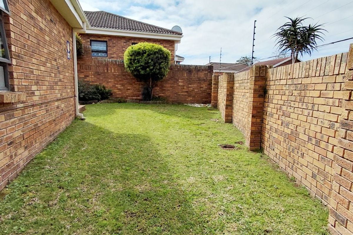 A private rear garden area featuring a well-maintained lawn enclosed by sturdy brick boundary walls with integrated electric security fencing.