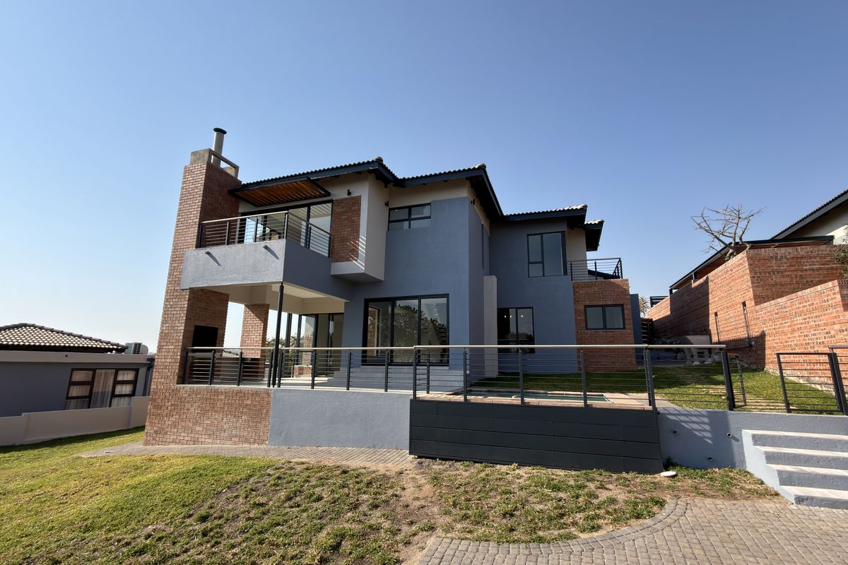 Rear view of a modern multi-story home featuring a brick chimney, balcony, paved patio area, and landscaped garden.