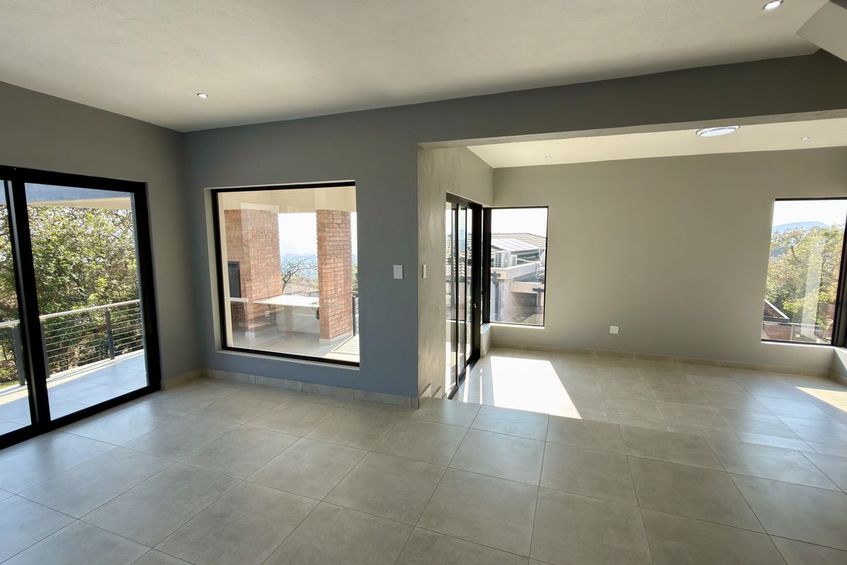 A bright, open-plan living area featuring neutral tiled flooring, modern recessed lighting, and large windows providing ample natural light and views.