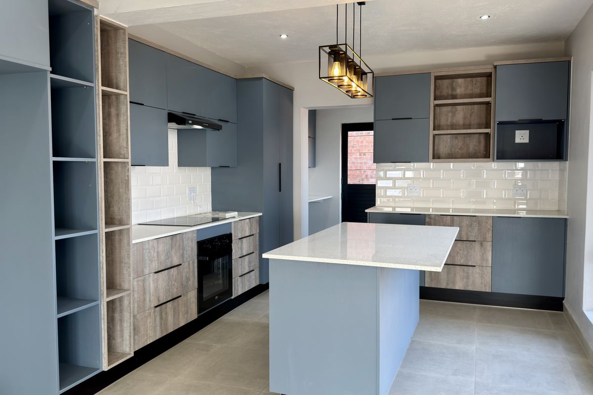 Modern kitchen featuring blue and wood-tone cabinetry, stone countertops, a central island, subway tile backsplash, and integrated appliances.