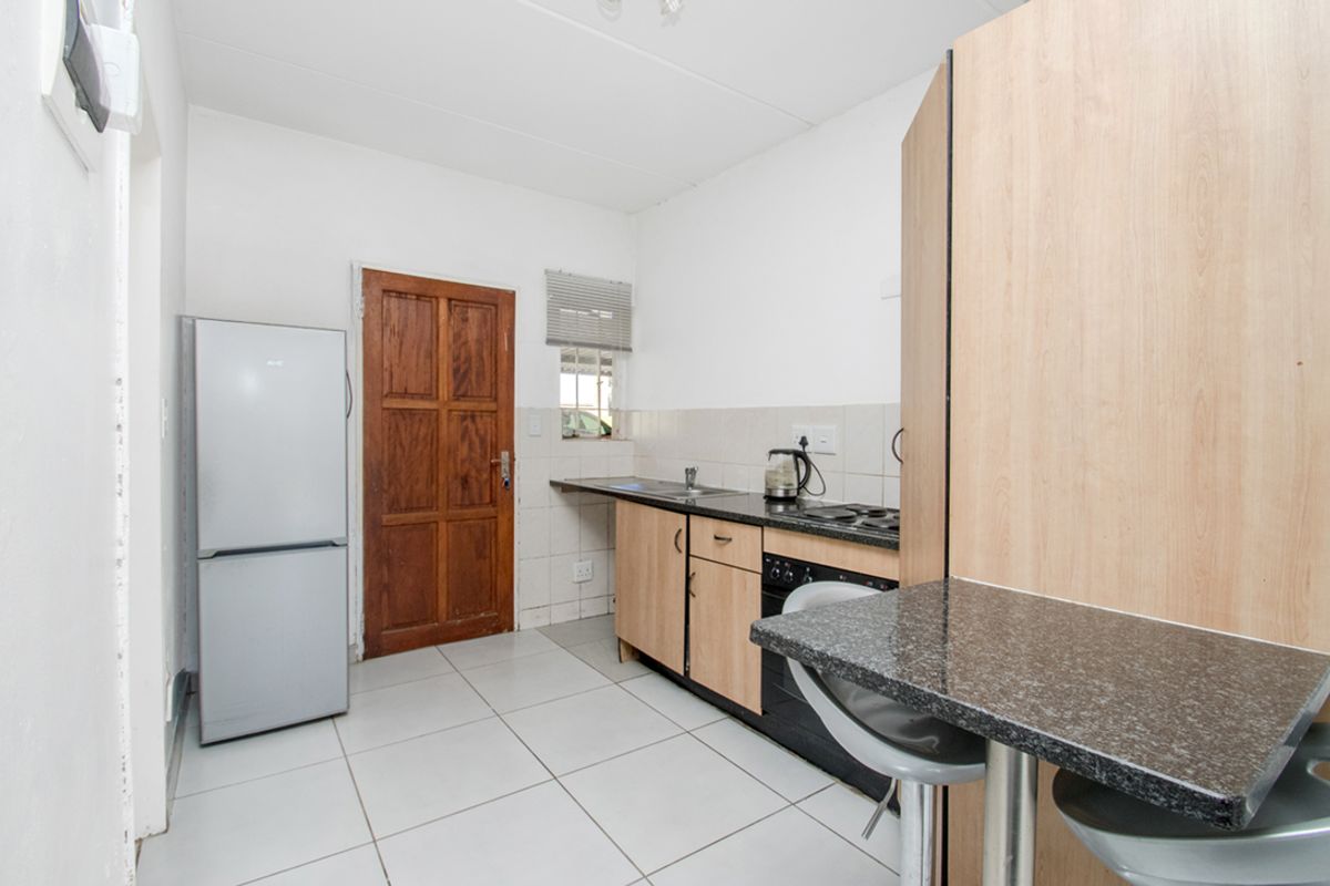A functional kitchen featuring built-in cabinetry, granite countertops, a stainless steel sink, and a built-in oven with hob, finished with tiled flooring.