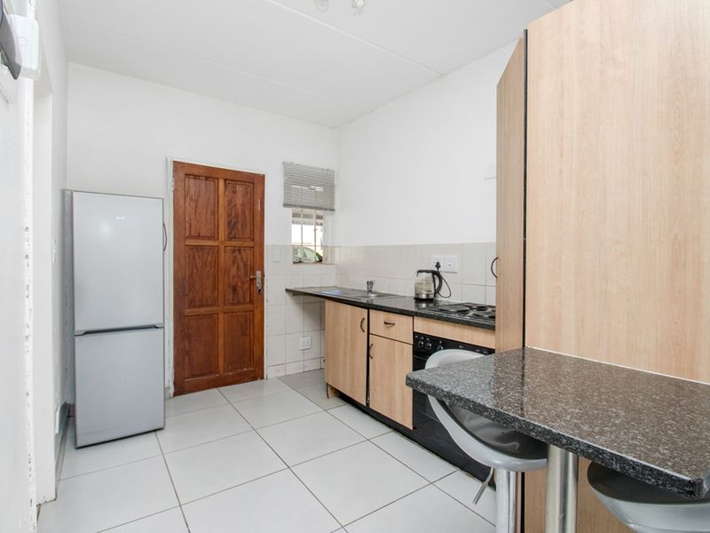 A functional kitchen featuring built-in cabinetry, granite countertops, a stainless steel sink, and a built-in oven with hob, finished with tiled flooring.