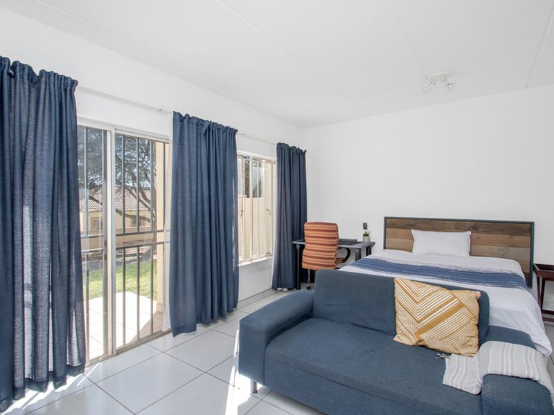 A bright bedroom featuring tiled flooring, large windows, and a sliding glass door providing access to the exterior.
