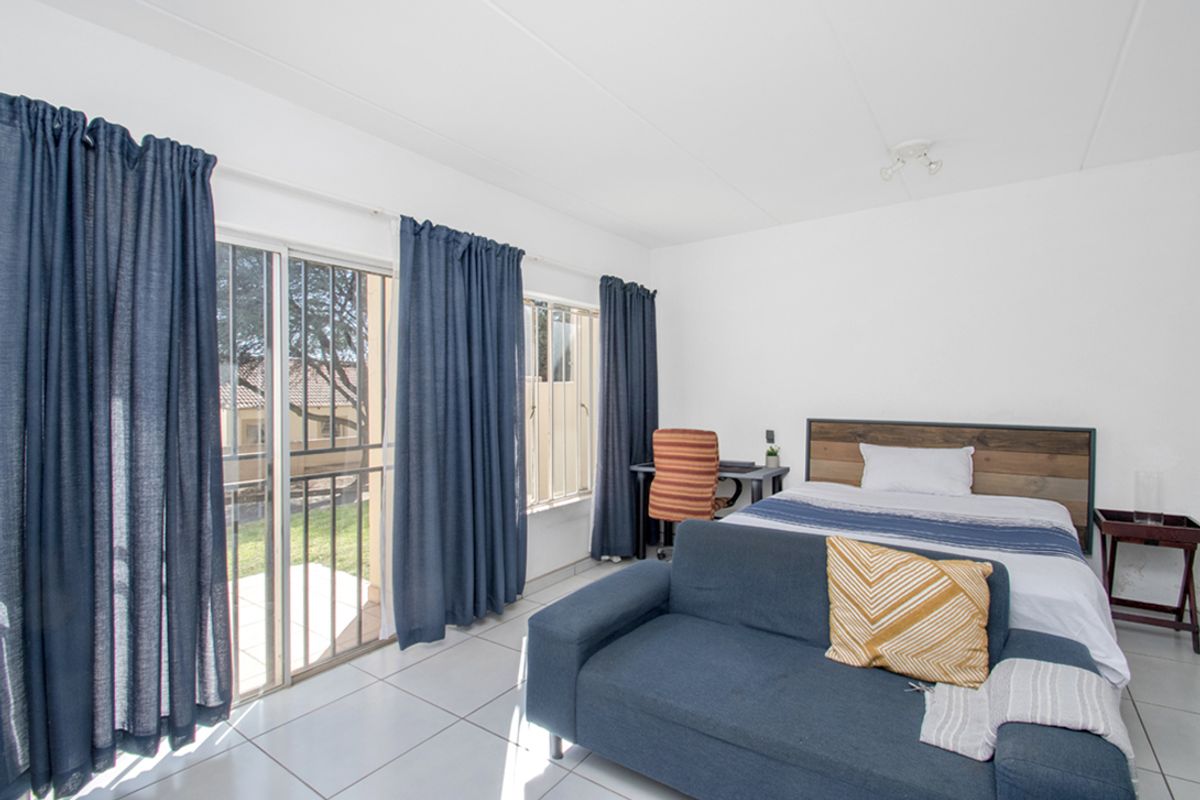 A bright bedroom featuring tiled flooring, large windows, and a sliding glass door providing access to the exterior.