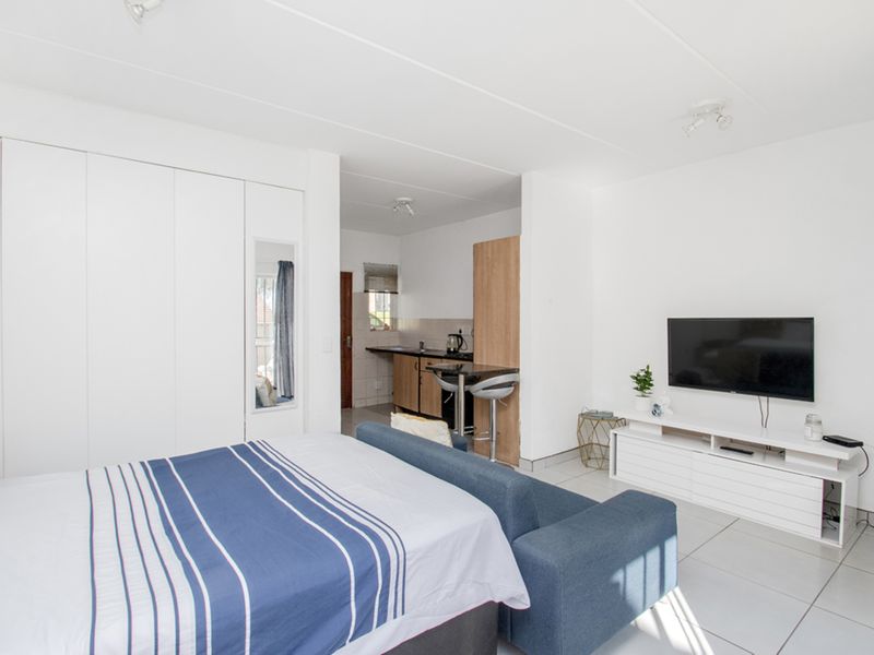 An open-plan studio apartment featuring a combined living and sleeping area with built-in cupboards and a compact kitchenette.