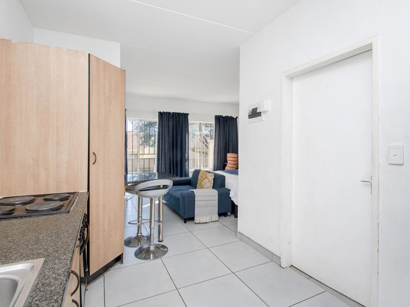 Open-plan apartment layout featuring a compact kitchen with granite countertops and electric hob, flowing into a combined living and sleeping area with balcony access.