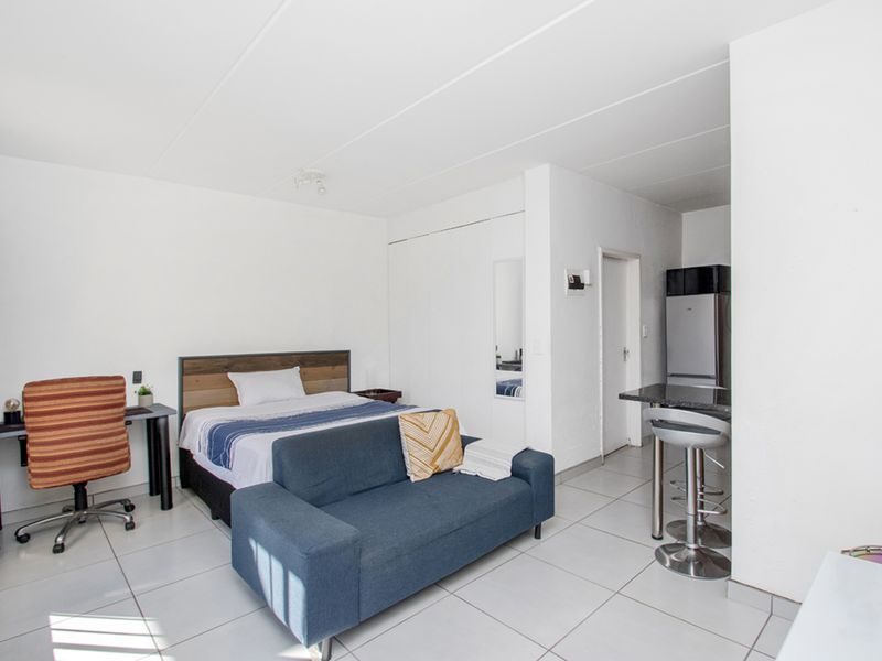 Open-plan studio apartment featuring tiled flooring, a breakfast counter, and built-in storage, offering a functional living and sleeping space.