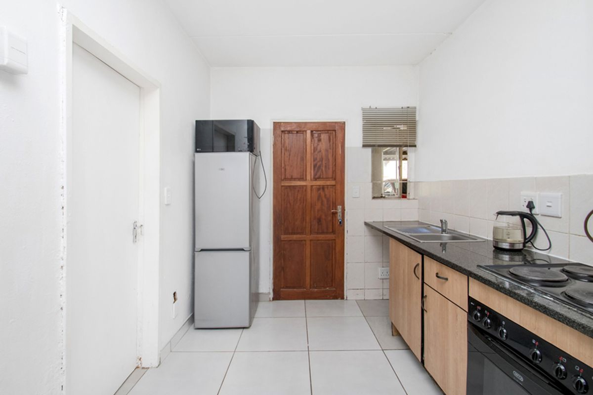 A functional kitchen featuring built-in cabinetry, granite countertops, a stainless steel sink, and a built-in oven with an electric hob.