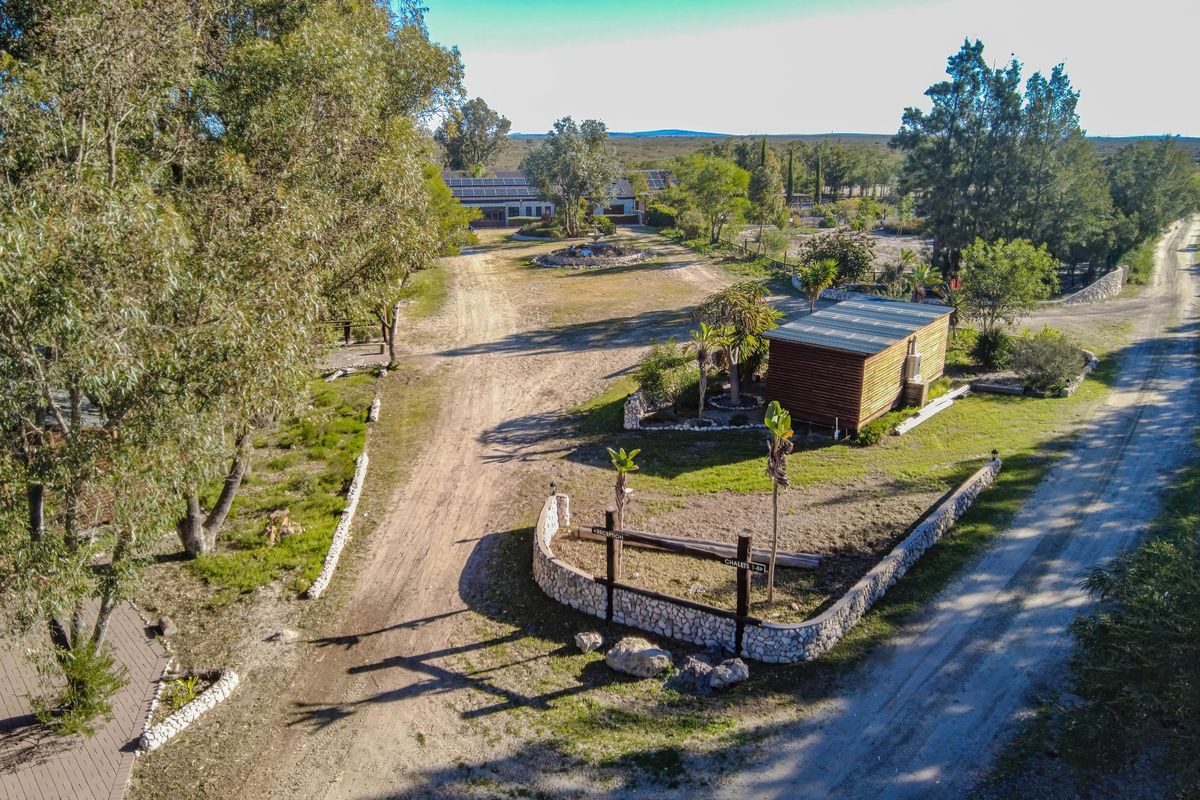 Aerial view of a farm property featuring a gravel driveway, stone boundary walls, a timber cabin, and a main building with solar panels.