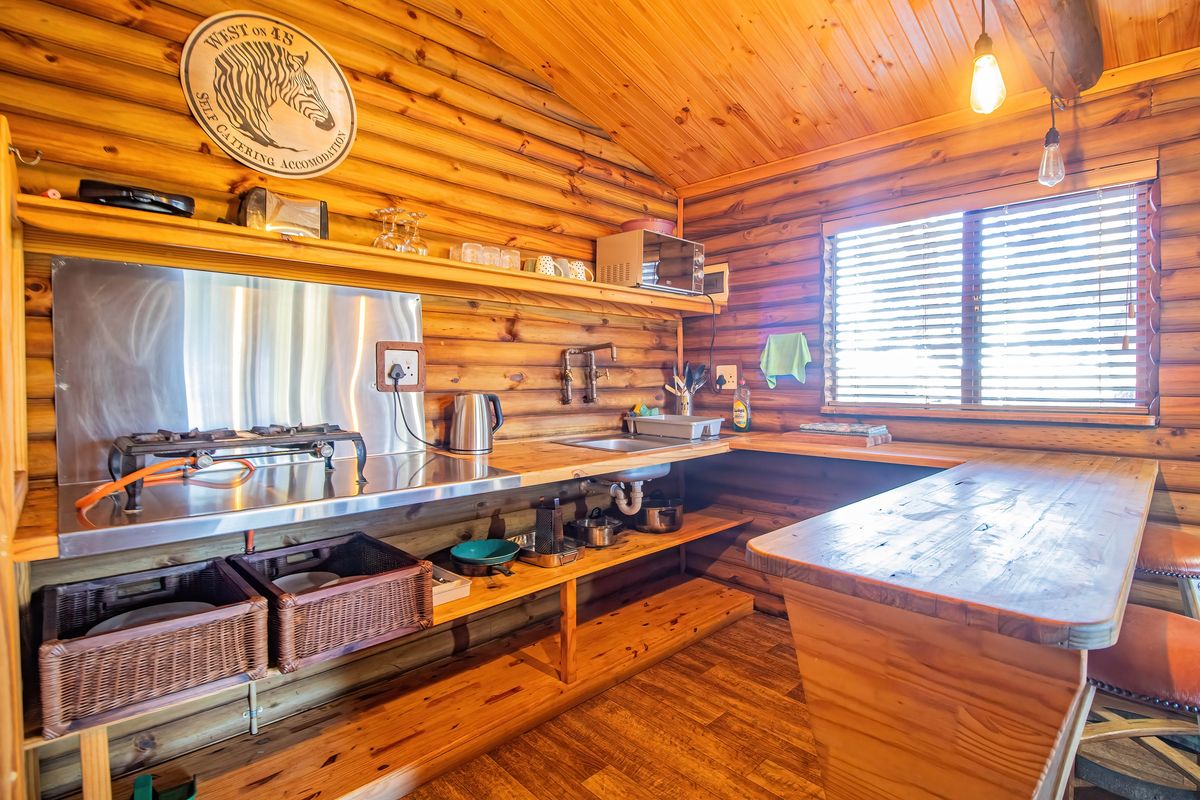 Rustic timber kitchen featuring a gas hob, stainless steel splashback, integrated sink, and a built-in timber breakfast bar with warm wood finishes.