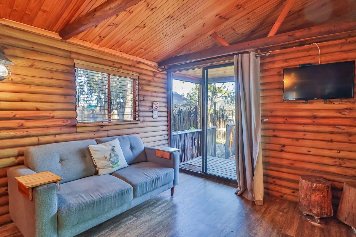 Cozy living room featuring rustic log cabin walls, exposed timber ceiling beams, and a sliding glass door providing access to an outdoor deck area.