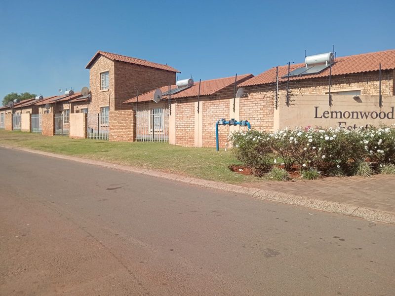 Street view of the Lemonwood Estate entrance, featuring face-brick cluster homes with solar geysers and perimeter electric fencing.