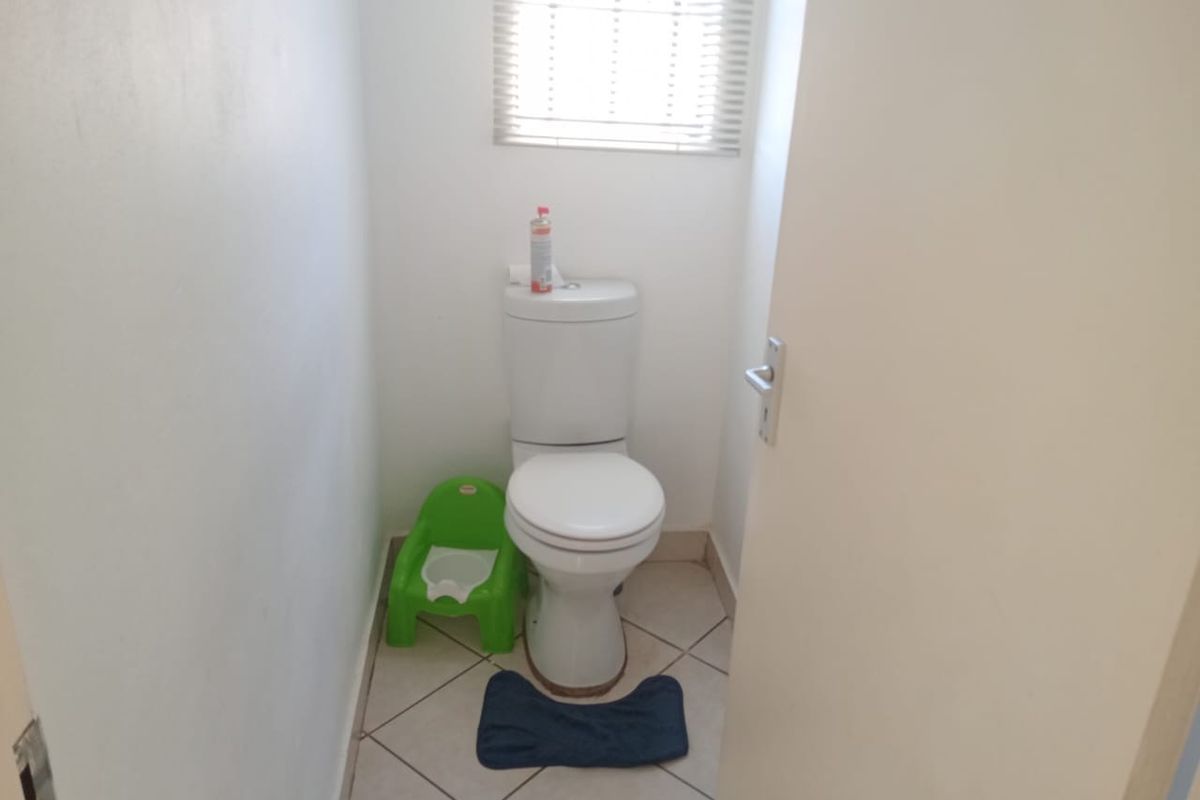 A compact guest bathroom featuring a standard toilet, tiled flooring, and a window with fitted blinds.