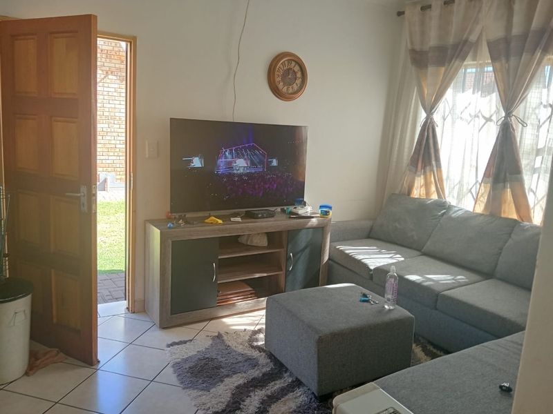 A functional living room featuring tiled flooring, natural light through window security bars, and direct access to the exterior via a wooden door.