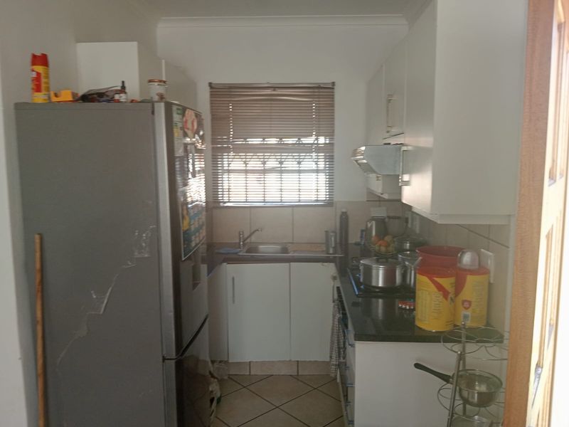 Compact kitchen featuring built-in cabinetry, granite countertops, a stainless steel sink, and an extractor fan, with tiled flooring and natural light.