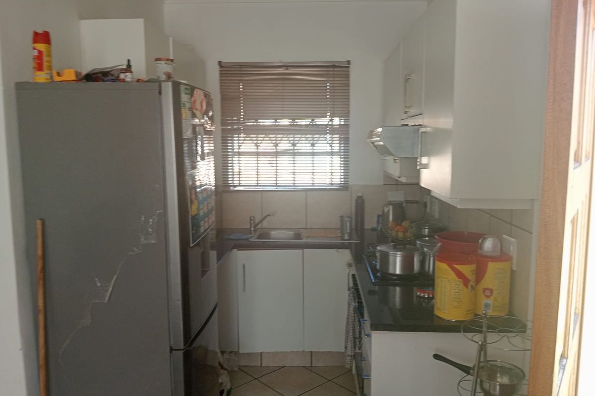 Compact kitchen featuring built-in cabinetry, granite countertops, a stainless steel sink, and an extractor fan, with tiled flooring and natural light.