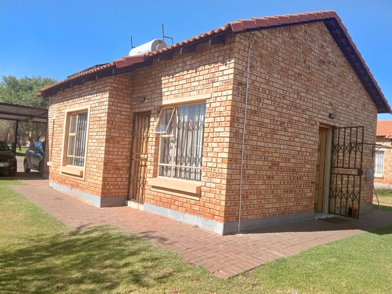 A well-maintained face-brick cluster home featuring a tiled roof, solar geyser, and secure entrance with paved surroundings.