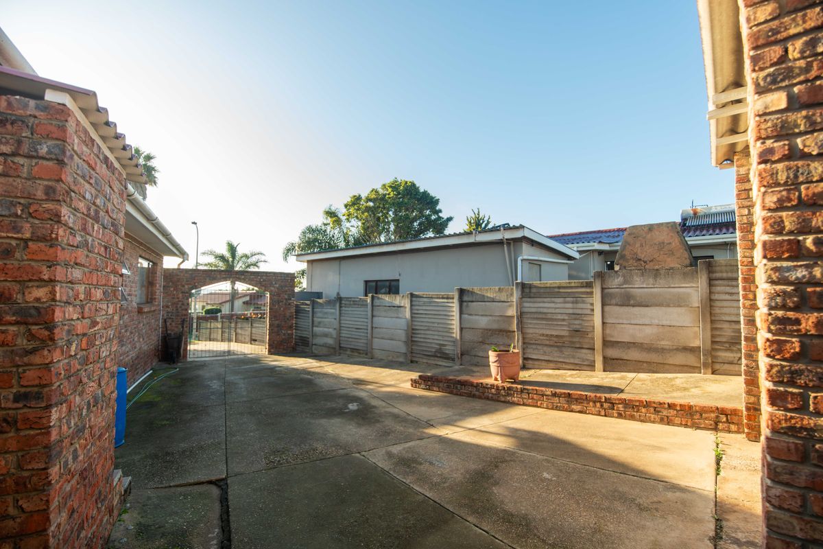 A rear exterior area featuring concrete paving, a brick archway with a metal gate, and a precast concrete boundary wall.