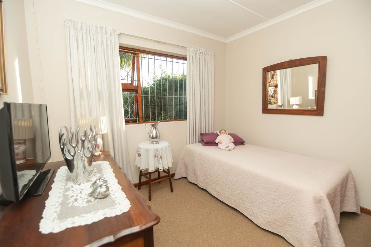 A cozy bedroom featuring neutral walls, carpet flooring, and a window fitted with security bars.