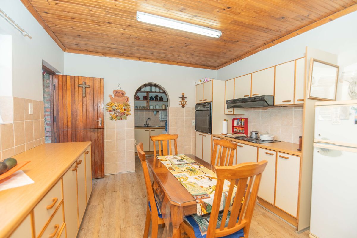 A dated kitchen featuring timber ceilings, built-in cabinetry, and an integrated oven, with an adjacent scullery area accessible through an arched doorway.