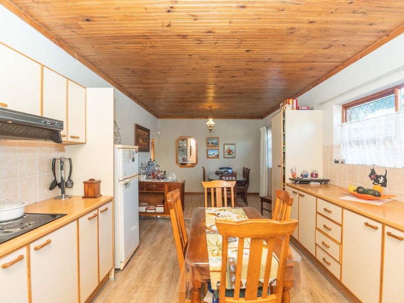 Open-plan kitchen and dining area featuring timber ceiling, laminate flooring, and dated cabinetry with an integrated electric hob and extractor fan.