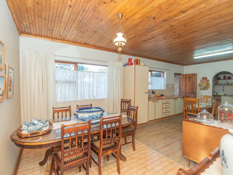 Open-plan dining and kitchen area featuring a timber-clad ceiling, tiled and laminate flooring, and traditional cabinetry with an arched transition to a scullery area.