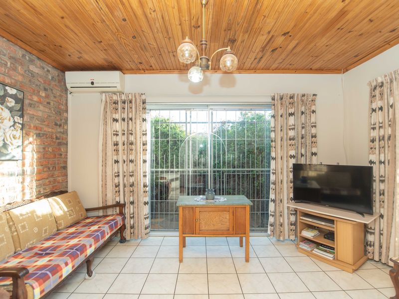 Living room featuring a timber ceiling, exposed brick feature wall, tiled flooring, and a sliding glass door with security gate leading to the exterior.