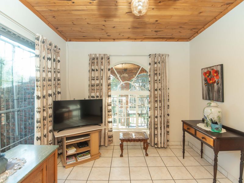A living room featuring a timber tongue and groove ceiling, ceramic floor tiles, and an arched window with security gate.
