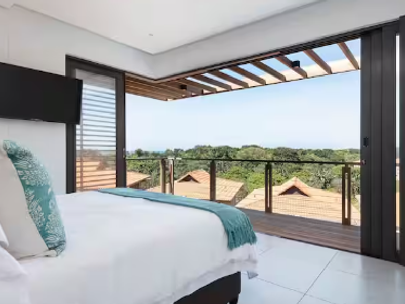 Modern bedroom featuring large sliding glass doors opening onto a private balcony with a timber pergola and scenic views.