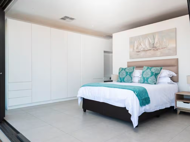 A modern, well-maintained bedroom featuring extensive built-in cabinetry, large sliding glass doors opening to the exterior, and neutral tiled flooring.