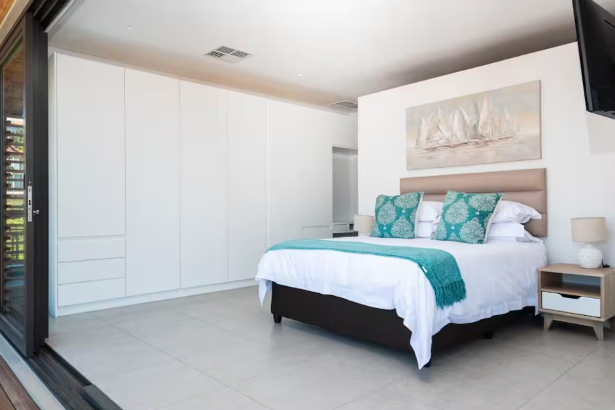 A modern, well-maintained bedroom featuring extensive built-in cabinetry, large sliding glass doors opening to the exterior, and neutral tiled flooring.