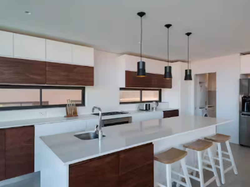 Modern kitchen featuring a large island with quartz countertops, two-tone cabinetry, integrated appliances, and stylish pendant lighting, with an adjacent scullery area.