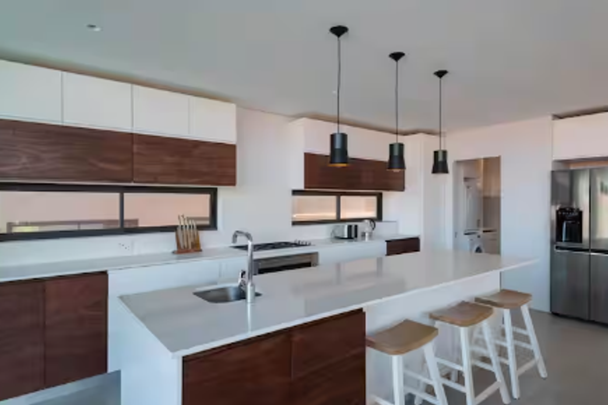 Modern kitchen featuring a large island with quartz countertops, two-tone cabinetry, integrated appliances, and stylish pendant lighting, with an adjacent scullery area.