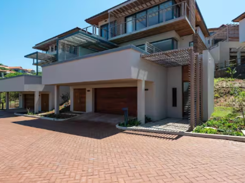 Modern multi-level residential facade featuring a paved driveway, double garage with timber doors, and architectural timber pergola detailing.